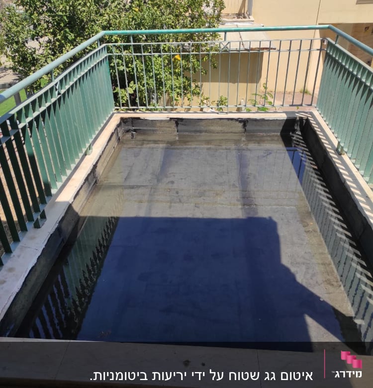 בריכה מרובעת עם מים, מוקפת מעקה מתכת ירוק